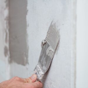man hand with trowel plastering a wall, skim coating plaster walls.